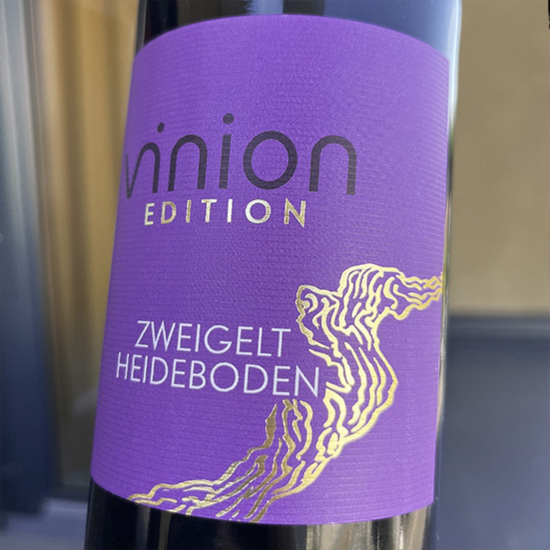 Nahaufnahme einer Vinion Edition Zweigelt Heideboden Weinflasche mit violettem Etikett und goldener Linienillustration.