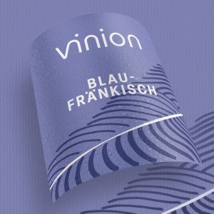 Gebogenes Vinion Blaufränkisch Etikett in Violettblau mit grafischem Linienmuster und Wassertropfen.