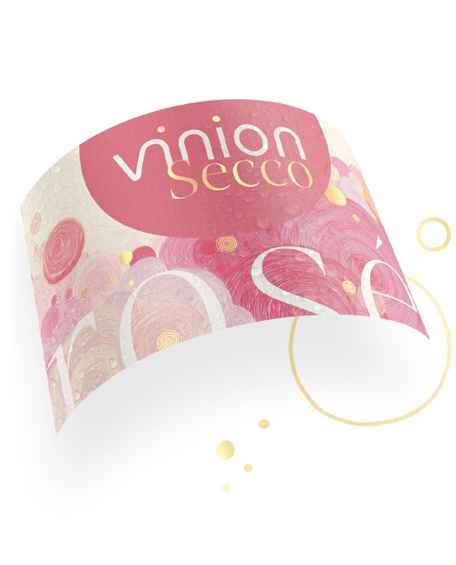 Gebogenes Vinion Secco Etikett mit rosa Muster, goldenen Details und weisser Schrift auf hellem Hintergrund.